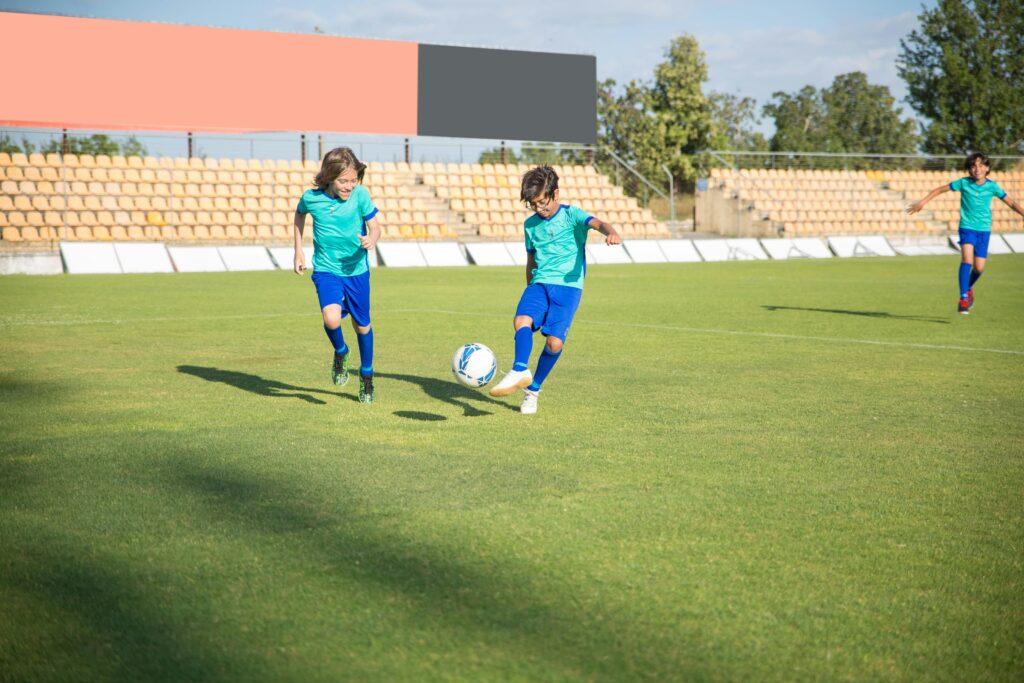 Children playing football on a sunny day in a Portuguese stadium.